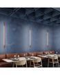 Sfeerfoto van drie smalle okerrode wandlampen Sappo van 150 cm lang met LED voor indirect licht in een restaurant
