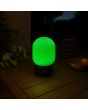 Sfeerfoto van de met groen licht brandende Brilliant Sarastro zwarte kunststof oplaadbare tafellamp voor buiten met wit ribbelglazen ovale kap met een hoogte van 20 cm en een diameter van 13 cm op een houten tuintafel