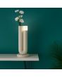 Sfeerfoto van de Brilliant Sayu beige oplaadbare tafellamp van 26,8 cm hoog in U vorm met vaas in 1 poot en een LED unit op de andere op een beige wandtafeltje