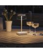 Sfeerfoto van Konstsmide Scilla witte tafellamp voor buiten op batterijen met transparant glazen kap met touch dimmer op een houten tuintafel met twee sorbet ijsjes