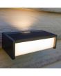 Sfeerfoto van bovenaf van Lutec Telis antraciet grijze wandlamp voor buiten van 18 cm breed met zonnepaneel bovenop en wit kunststof venster naar beneden en voren en klein venstertje naar boven