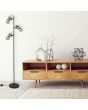 Trio Tosh 404300332 sfeerfoto van zwarte vloerlamp met drie cilindervormige spots met een houten achterzijde en zwart gaas voor naast een kastje met drie laden