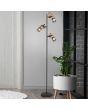 Trio Tosh 404300332 sfeerfoto van zwarte vloerlamp met drie cilindervormige spots met een houten achterzijde en zwart gaas voor naast een kamerplant