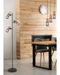 Trio Tosh 404300332 sfeerfoto van zwarte vloerlamp met drie cilindervormige spots met een houten achterzijde en zwart gaas voor naast een houten wand en een drie-lichts hanglamp uit dezelfde serie