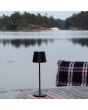 Sfeerfoto van Konstsmide Vence mat zwarte tafellamp voor buiten van 32 cm hoog met touchdimmer op de kop op een tuintafel voor een meertje