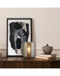Sfeerfoto van Searchlight Zweden tafellamp van 26cm hoog met mokkabruine lampvoet en cilindervormig amberkleurig glazen kap op een houten kastje met boeken en een schilderij
